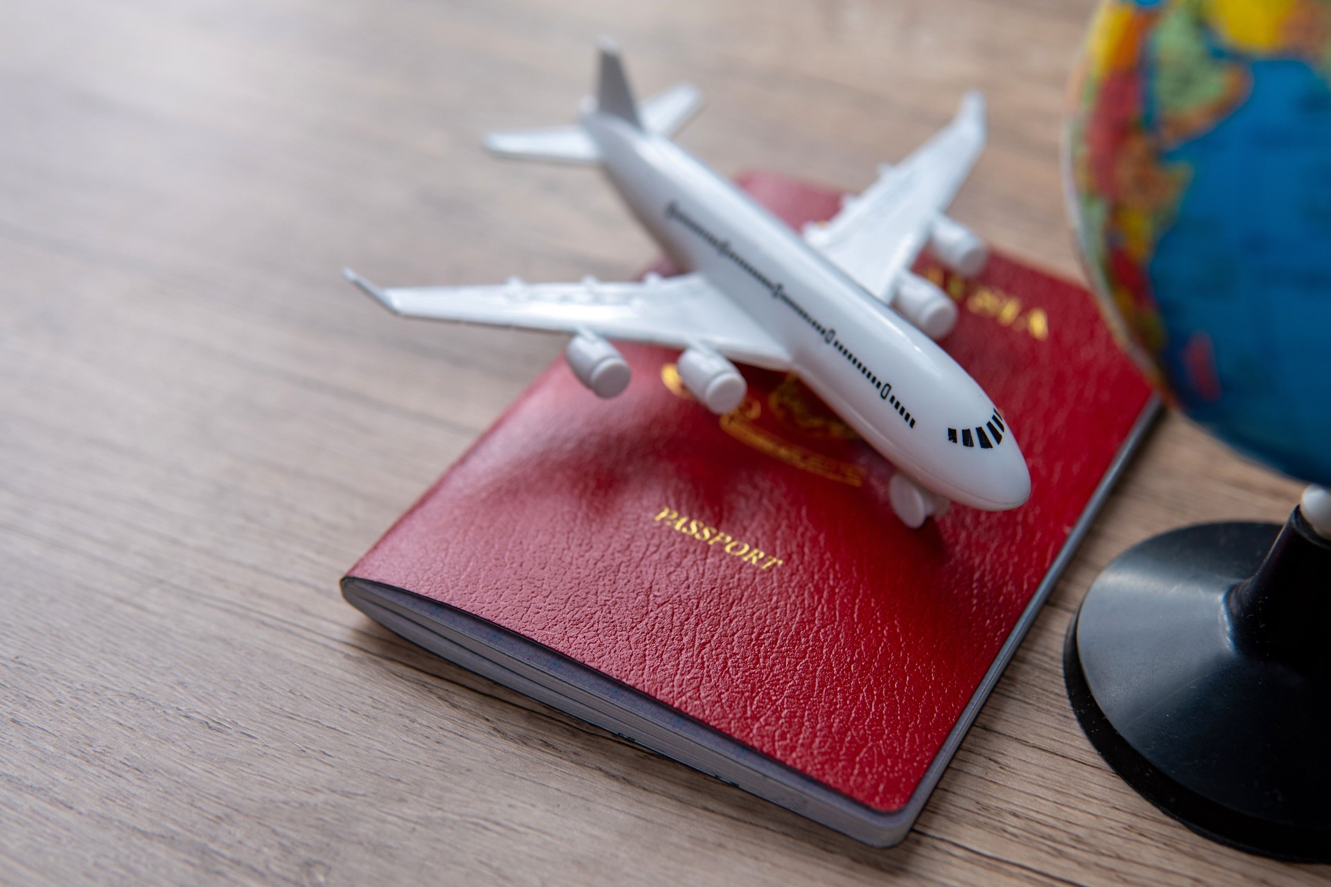 A small model airplane on top of a passport and next to a small globe.